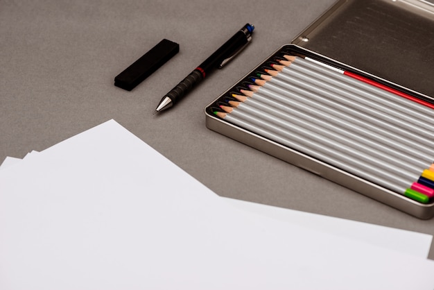 Lápices de colores, bolígrafo, papel sobre mesa gris