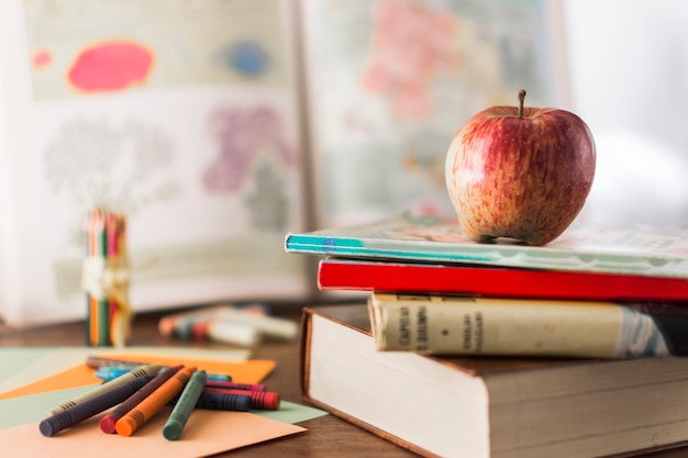 Lápices de colores cerca de libros y manzana