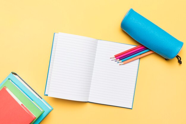 Lápices de colores compuestos en cuaderno abierto con páginas vacías