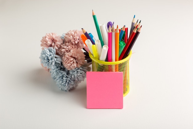 Lápices de colores de vista frontal con flores en el escritorio blanco