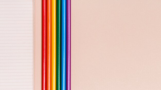 Lápices y cuaderno coloridos del arco iris en fondo beige
