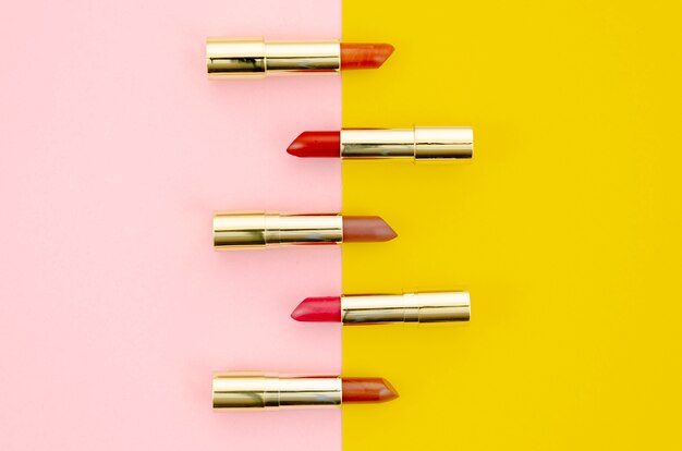 Lápices labiales de diferentes colores sobre fondo rosa y amarillo