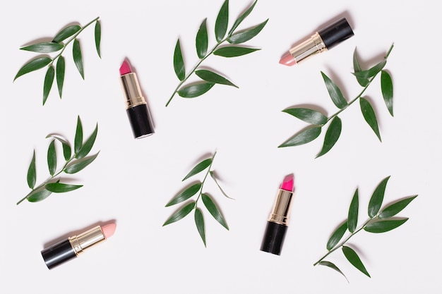 Lápices labiales y ramas de plantas en blanco