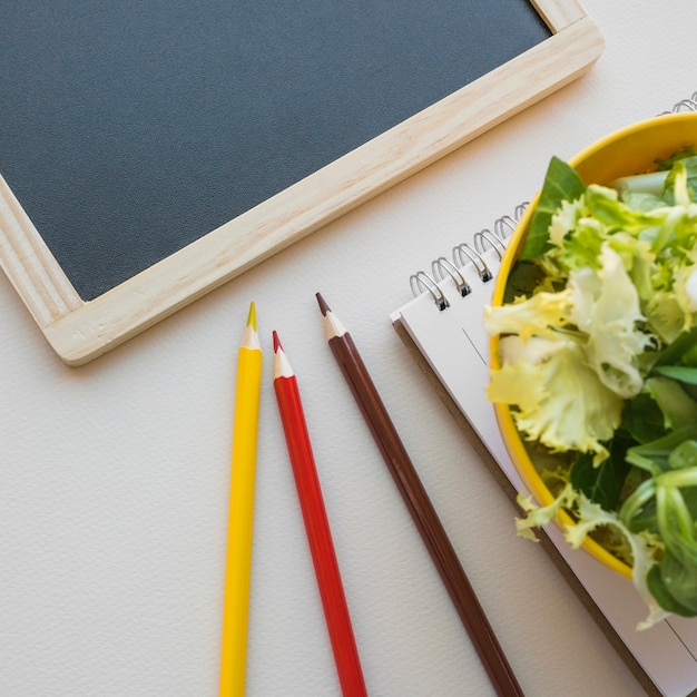 Foto gratuita lápices de primer plano cerca de la pizarra y ensalada