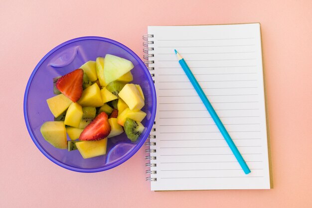 Lápiz y bloc de notas cerca de ensalada de frutas