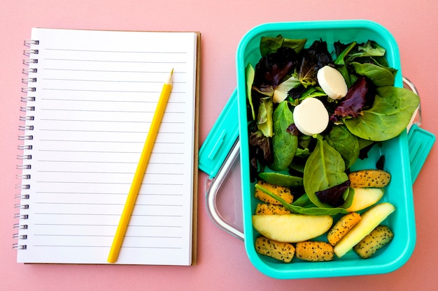 Lápiz y cuaderno cerca de la ensalada