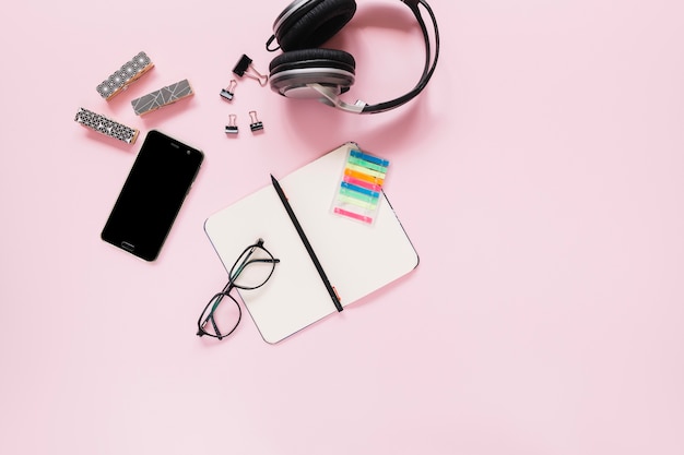 Lápiz en diario en blanco; los anteojos; y papelería con teléfono móvil en fondo rosa