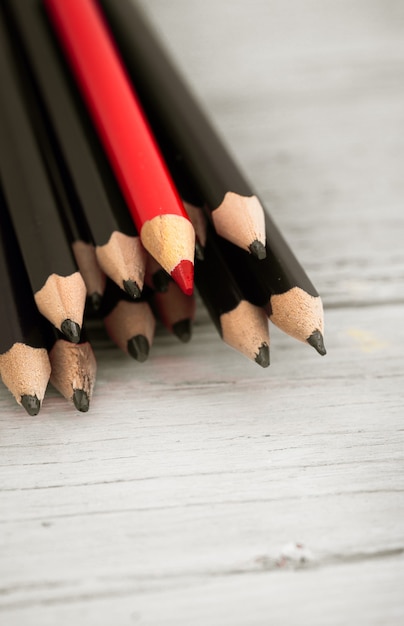 El lápiz rojo se destaca entre la multitud de lápiz negro sobre un fondo blanco de madera.