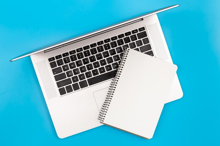 Foto gratuito laptop y bloc de notas en blanco en una vista superior de fondo azul