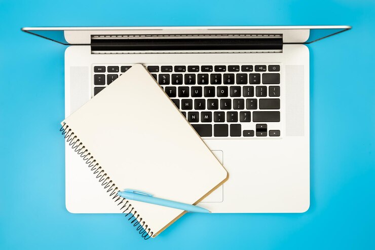 Foto gratuito laptop y bloc de notas en un fondo plano azul