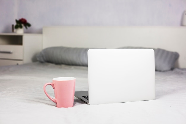 Laptop en cama blanca con taza de café