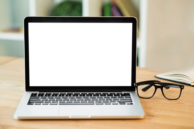 Laptop con pantalla blanca en blanco y lentes en escritorio de madera