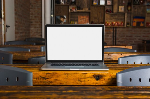 Laptop con pantalla blanca en mesa de madera en la cafetería.