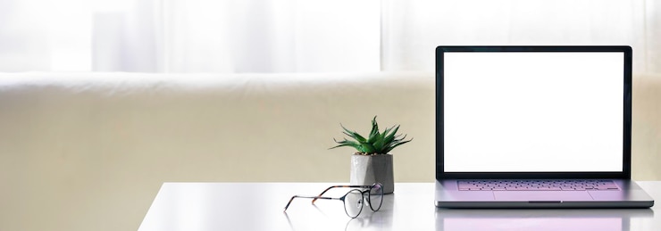 Foto gratuito laptop con una pantalla en blanco en una mesa blanca con una olla de flores y gafas