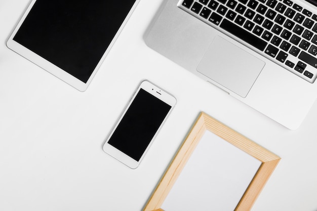 Laptop con smartphone y marco en blanco.