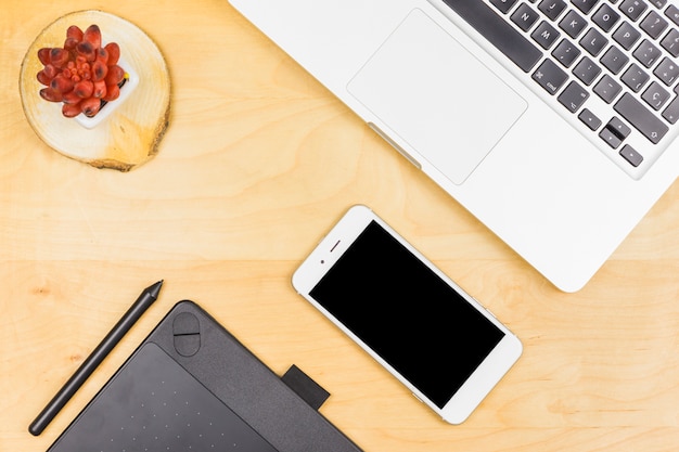 Laptop con smartphone y planta sobre mesa.