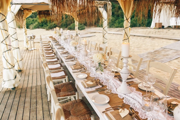 Larga mesa de cena blanca con cristalería y candleholders espumosos se encuentra en la playa