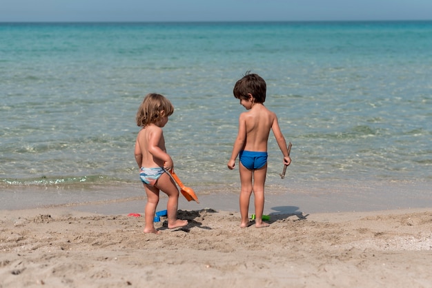 Larga vista de niños de pie en la playa con juguetes.