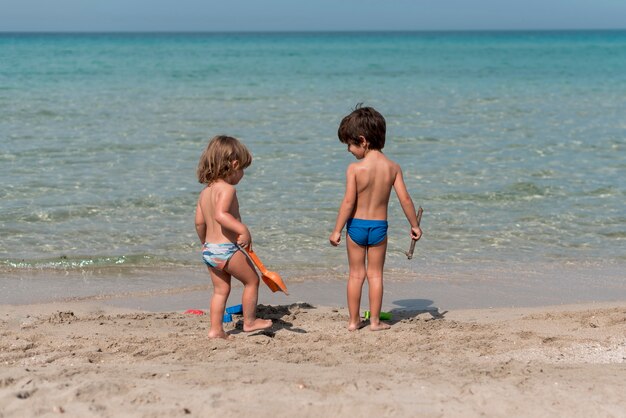 Larga vista de niños de pie en la playa con juguetes.