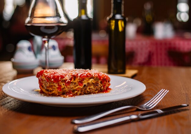 Lasaña italiana adornada con salsa de tomate y parmesano rallado servido con vino tinto