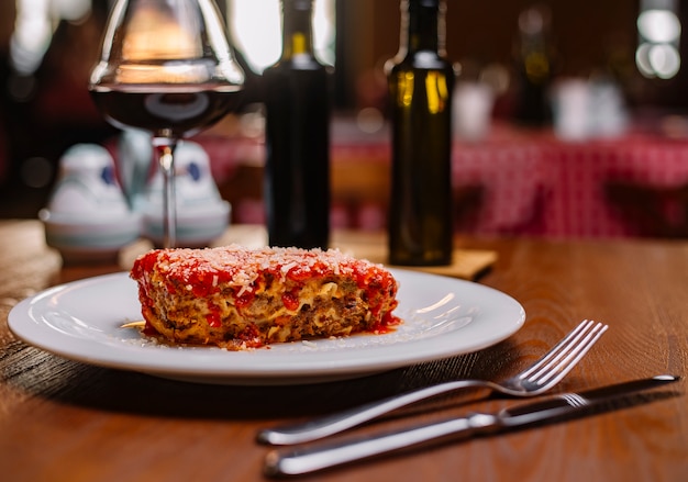 Lasaña italiana adornada con salsa de tomate y parmesano rallado servido con vino tinto