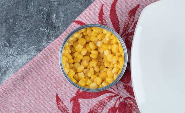 Una lata llena de semillas de palomitas de maíz con plato vacío sobre el mantel.