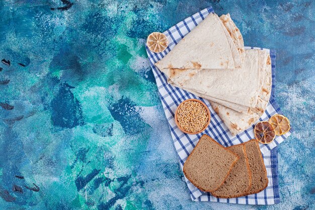 Lavash y rebanadas de pan sobre un paño de cocina, sobre la mesa azul.