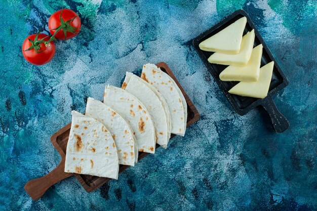 Lavash en una tabla y delicioso queso en una tabla junto a los tomates, sobre el fondo azul.