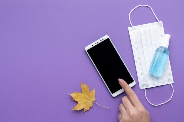 Lay Flat de mano con smartphone con máscara médica y hoja de otoño