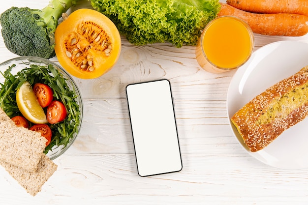 Foto gratuita lay flat de teléfono inteligente con comida y pan