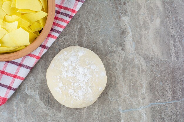 Un lazo de láminas de masa junto a la masa sobre un paño de cocina sobre mármol.