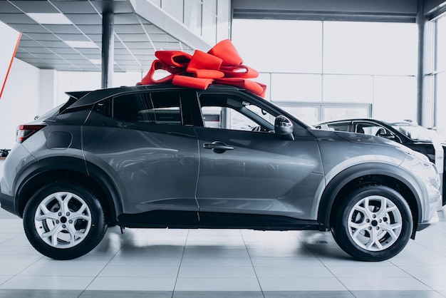 Foto gratuita lazo rojo en un coche nuevo como presente de pie en la sala de exposición de coches