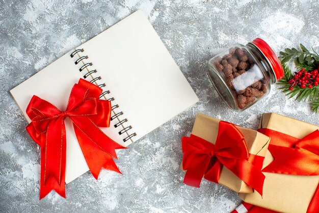 Lazo rojo de la vista superior en cereal del cuaderno en los regalos de navidad de las ramas del árbol de navidad del tarro en la tabla gris