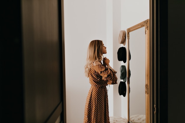 Lazos de mujer joven se inclinan sobre su elegante vestido. Chica mira en el espejo antes de ir a una cita romántica.