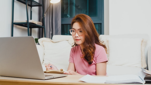 Lección de aprendizaje a distancia de joven estudiante adolescente de asia con profesor en línea y estudio en computadora portátil en la sala de estar de casa por la noche. distanciamiento social, cuarentena para la prevención del coronavirus.