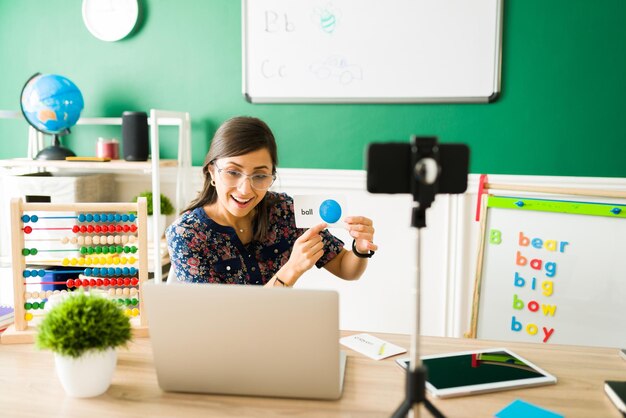 Lecciones de vocabulario. Maestra feliz usando tarjetas para enseñar las letras y el alfabeto a niños pequeños en edad preescolar durante una clase virtual