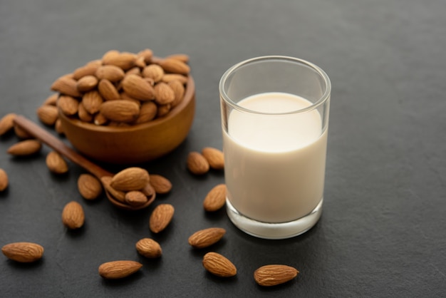 Leche de almendras con almendras en una cuchara de madera y cuenco sobre fondo negro.