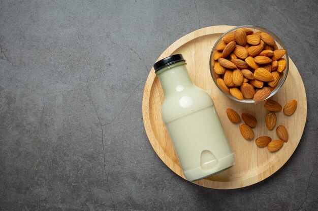 Leche de almendras en botella con almendras sobre fondo oscuro