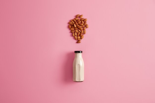 Leche de almendras recién hecha en botella de vidrio para sustituir los productos lácteos por los vegetarianos. Fondo rosado, vista superior. Bebida natural vegetariana saludable. Dieta, cuidado de la salud, concepto de nutrición adecuada