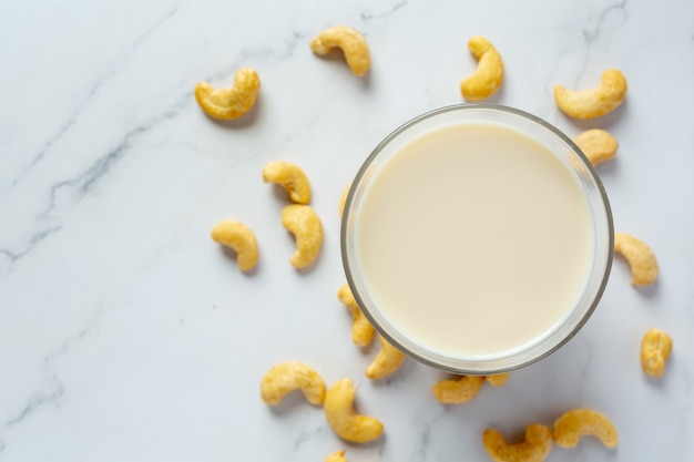 Leche de anacardo vegana en vaso con anacardos sobre fondo de mármol