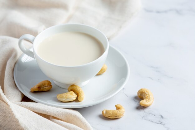 Leche de anacardo vegana en vaso con anacardos sobre fondo de mármol