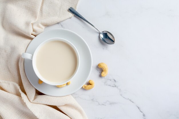 Leche de anacardo vegana en vaso con anacardos sobre fondo de mármol