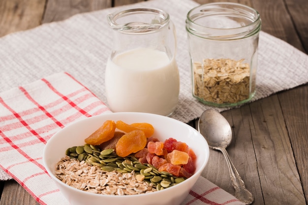 Foto gratuita leche con copos de avena, semillas de calabaza y frutas secas en el cuenco en la mesa de madera