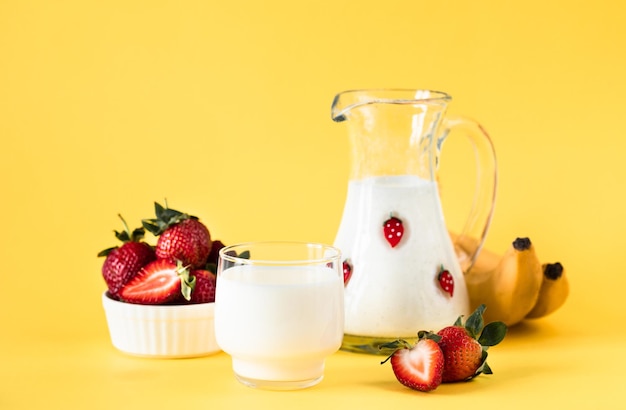 Leche fresas y plátanos frescos sobre un fondo amarillo dieta saludable y estilo de vida nutricional