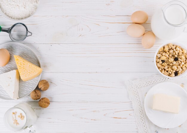 Leche; huevos; tazón de cereales queso; Harina y nueces en mesa de madera blanca