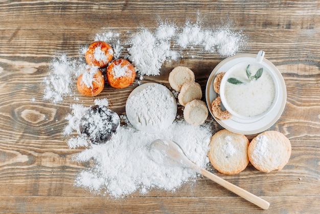 Leche picante con menta, galletas, cuchara, azúcar en polvo en una taza sobre superficie de madera, superficie plana.