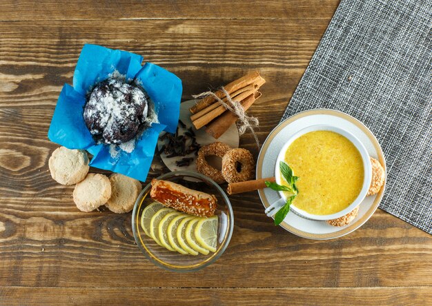 Leche picante en una taza con menta, galletas, clavo, rodajas de limón, canela, vista superior en mesa de madera