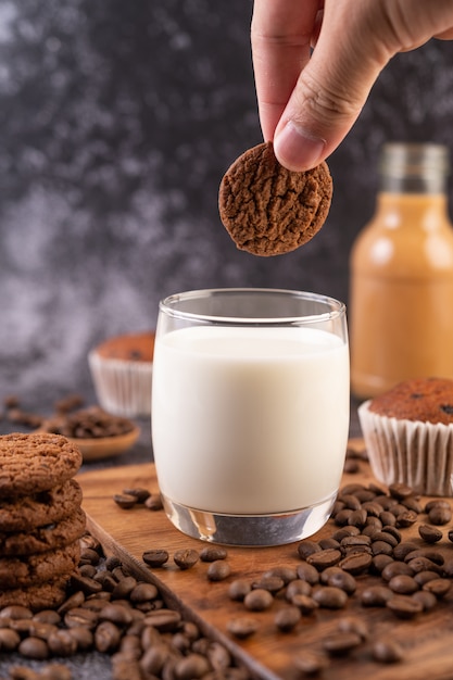 Leche en un vaso, completa con granos de café, pastelitos, plátanos y galletas en un plato de madera.