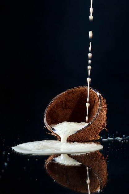 Foto gratuita leche vertiendo en la mitad de coco sobre la pared negra