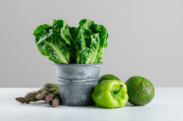 Lechuga en un mini cubo con espárragos, pimiento, aguacate en mesa blanca y gris